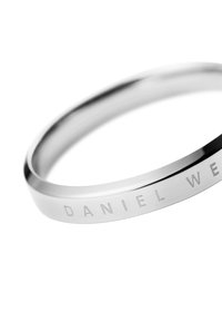 Silver stainless steel bangle with a smooth, polished finish, featuring engraved lettering on one side. Lightweight, circular shape.