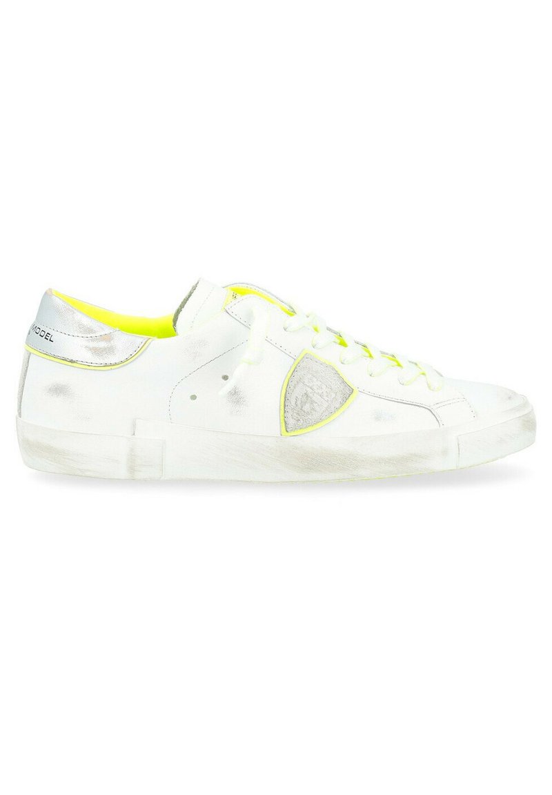 Sneakers bianchi con un accento argentato lucido sul tallone, interno giallo neon, punta rotonda e suola in gomma testurizzata. I lacci sono bianchi.