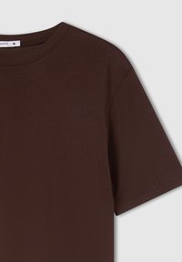 Brązowy bawełniany T-shirt z okrągłym dekoltem, krótkimi rękawami i gładką fakturą. Metka pokazuje rozmiar "S" przy dekolcie.