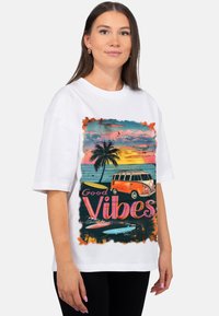 Wit oversized T-shirt met een kleurrijke grafische print van een vintage bestelwagen, palmboom, zonsondergang en de tekst "Good Vibes."