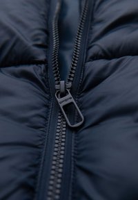 Giacca puffer blu navy con una zip metallica visibile, dotata di un tirazip rotondo e un tessuto trapuntato.