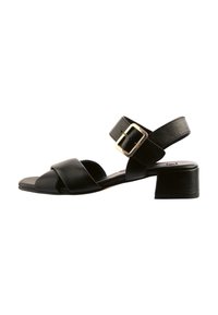 Černé kožené sandály s nízkým blokovým podpatkem, širokými kříženými pásky, nastavitelným páskem kolem kotníku a zlatým detailním sponou.
