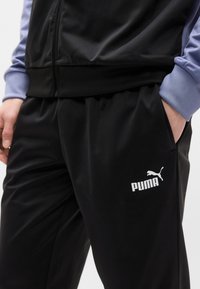 Μαύρο αθλητικό παντελόνι από λείο ύφασμα με ελαστική μέση. Διαθέτει λευκό λογότυπο Puma στο αριστερό μηρό και μωβ αντίθετες μανσέτες.