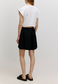 Top bianco corto con maniche corte, abbinato a una gonna nera plissettata. Modella con sandali neri a fascia. Design semplice e pulito.