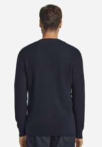 Marinblå stickad tröja med en strukturerad tyg, långa ärmar och rundad halsringning. Bakpartiet har en slät yta och ribbade manschetter.