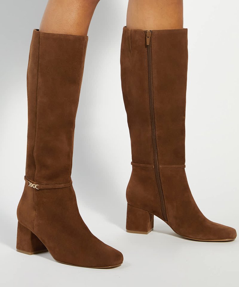 Bottes montantes en daim marron avec talons blocs, fermeture éclair latérale et petit détail décoratif en chaîne près de la cheville.