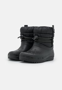 Bottes noires imperméables avec une semelle en caoutchouc texturé, un haut rembourré, un cordon élastique et des trous d'aération pour la ventilation.