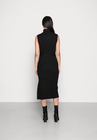 Abito in maglia a coste nera con colletto alto e design senza maniche, caratterizzato da una silhouette aderente e un orlo dritto, abbinato a stivaletti neri alla caviglia.
