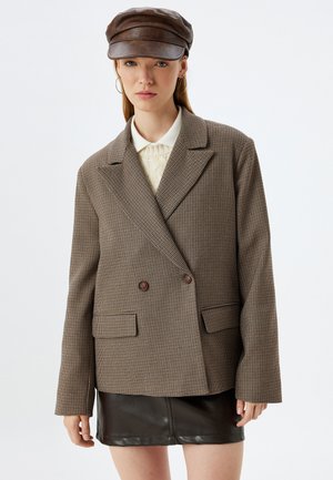 Braun kariertes Blazer mit doppelter Knopfleiste, Reverskragen, zwei vorderen Taschen und kontrastierenden dunklen Knöpfen, kombiniert mit einem schwarzen Lederrock.