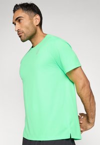 Πράσινο αθλητικό μπλουζάκι με κοντά μανίκια, στρογγυλή λαιμόκοψη και λεπτή υφή. Διαθέτει μικρό λογότυπο στο στήθος και ανοίγματα στις πλευρές στο τελείωμα.