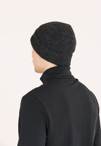 Strikket hue i mørkegrå med ribbet tekstur, tæt pasform og rund top. Båret med en sort højhalset bluse. Bagfra vist.