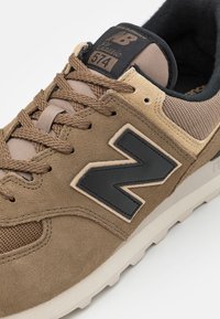 Baskets en daim marron avec panneaux en mesh, arborant un grand logo "N" noir. Design à lacets, col rembourré et semelle en caoutchouc.