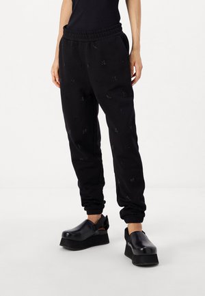 Zwarte trainingsbroek met een elastische tailleband, voorzien van een subtiel patroon en met cuffed enkels, gecombineerd met zwarte platformklompen.