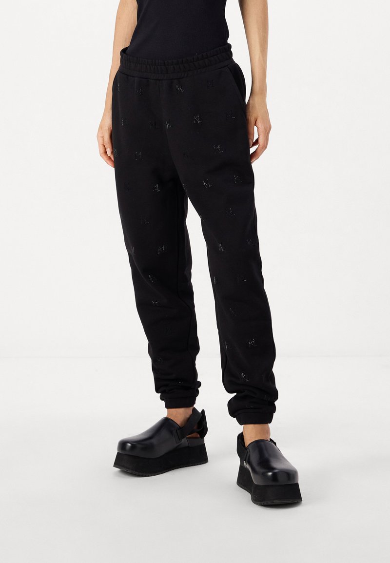 Svarta sweatpants med elastisk midja, med ett subtilt mönster och muddar vid anklarna, kombinerade med svarta plattformsskor.