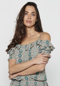 Top off-shoulder a fantasia floreale con maniche a volant. Presenta una combinazione di colori turchese e beige, realizzato in tessuto leggero.