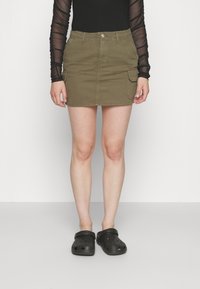 Olivenfarge denimskjørt med en tettsittende design, frontlukking med knapper og to sidelommer. Kombinert med svarte crocs.