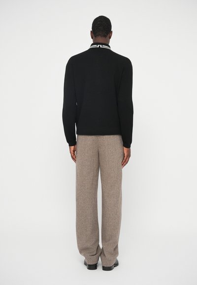 Musta neule, jossa on erottuva valkoinen kaulus, yhdistettynä beigeihin, teksturoituihin leveälahkeisiin housuihin ja mustiin kenkiin. Näkymä takaa.