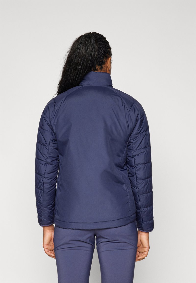 Veste matelassée marine avec col haut et épaules structurées ; présente des manches matelassées et un panneau arrière lisse, idéale pour le superposition.