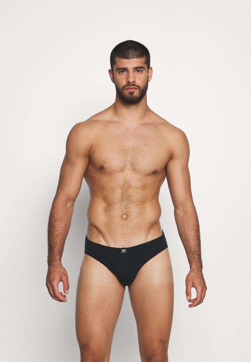 Boxers noirs avec une texture lisse et une coupe basse, arborant un logo discret sur la taille, portés par un mannequin masculin au physique athlétique.