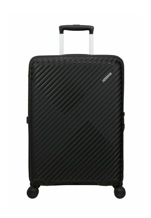 Valigia nera rigida con scanalature diagonali, maniglia telescopica estesa, quattro ruote girevoli e logo American Tourister nell'angolo in alto a destra.