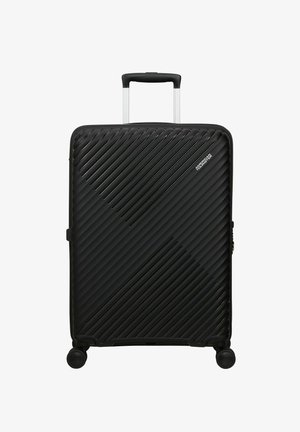 Valigia nera rigida con scanalature diagonali, maniglia telescopica estesa, quattro ruote girevoli e logo American Tourister nell'angolo in alto a destra.