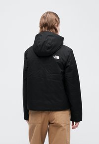 Černá kapuce s hladkým povrchem a logem The North Face na horní zadní části. Spárované s béžovými kalhotami a minimalistickým designem.