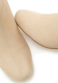Chaussures beiges en daim à bout pointu présentant une texture lisse avec des coutures minimales et une semelle plate, affichant un design épuré et simple.