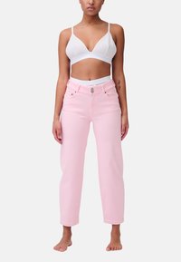 Jeans in denim rosa chiaro con vita alta, caratterizzati da un bottone argento e tasche frontali. Indossati con un bralette bianco.