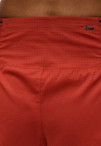 Κοντινό πλάνο κόκκινων αθλητικών σορτς με υφασμένο ύφασμα και μικρή οριζόντια τσέπη με φερμουάρ στη μέση.