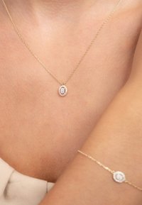 Collier en or avec un pendentif ovale doté d'une pierre précieuse centrale entourée de petits cristaux, accompagné d'un bracelet assorti.
