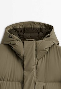 Veste matelassée vert olive avec col montant et capuche ajustable équipée de cordons de serrage des deux côtés.