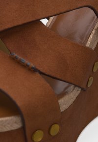 Καφέ σουέντ πλατφόρμα πέδιλο με σταυρωτούς ιμάντες, διακοσμητικές χάντρες, μπρούτζινες τριβές και πλεγμένο άκρο σόλας από τζούτ.