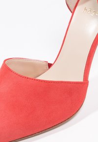 Chaussure à talons hauts en suede rouge avec un bout pointu et un dos ouvert, dotée d'une doublure intérieure lisse et d'un logo de marque discret sur la semelle.