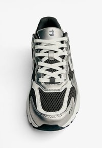 Sølv- og sorte atletiske sko med mesh-paneler, gummisål og hvide snørebånd. Har buet design og logo på tunge.