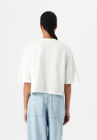 Cropped, white cotton t-shirt with short sleeves and a round neck, paired with light blue loose-fitting denim pants featuring back pockets.