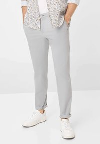 Pantaloni in cotone grigi chiari slim fit, con orli arrotolati e tasche laterali, abbinati a sneakers bianche e una camicia a fantasia.