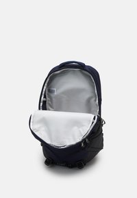 Zaino navy con interno grigio, dotato di manico superiore, chiusura con zip e fibbie esterne. Tessuto liscio con struttura rinforzata.