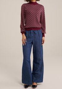 Burgundy mönstrad tröja med ribbad rundad hals; mörkblå vida denimbyxor med dragsko i midjan; svarta skor.