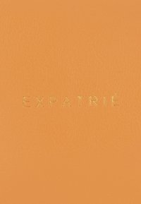 Materiale in pelle arancione con il testo impresso "EXPATRIÉ" in caratteri dorati, creando una superficie liscia e testurizzata.
