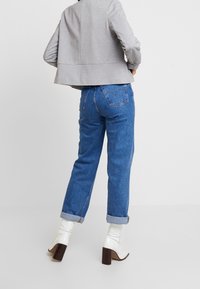 Harmaa lyhyt takki rentoa mitoitusta, yhdistettynä sinisiin farkkuihin. Valkoiset korkeat nilkkasaappaat täydentävät asukokonaisuuden.