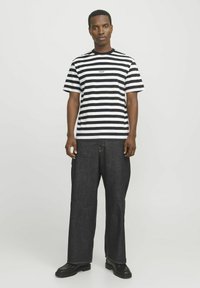 Sort-hvid stribet kortærmet t-shirt med rund hals, parret med brede mørke denimbukser og sorte platform-sko.