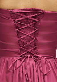 Πίσω μέρος στελέσματος χωρίς τιράντες σε μωβ απόχρωση με ραμμένο πάνελ και σατέν κορδόνι σε σταυρωτό σχέδιο δεμένο σε φιόγκο στη μέση.