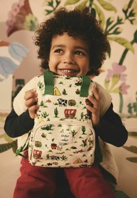 Malý batoh s béžovou tkaninou, zdobený barevnými kreslenými vzory. Zelené popruhy, přední kapsa a značka jsou viditelné.