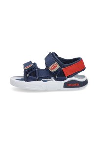 Sandalia azul marino con correas ajustables, suela blanca, parte superior de tela texturizada y acento rojo. Presenta una marca en el lateral.