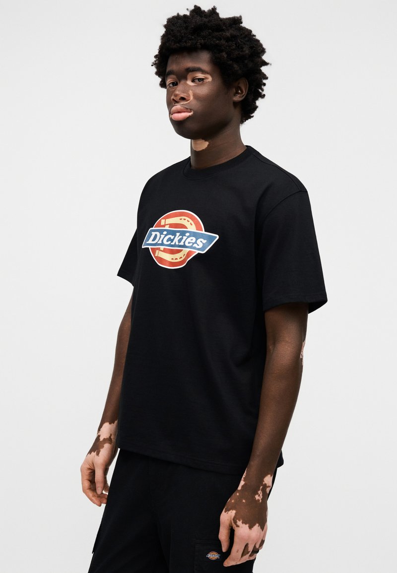 T-shirt nera a maniche corte con un colorato logo Dickies circolare sul davanti. Il tessuto appare morbido e casual.
