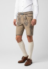 Brune læder lederhosen med indviklet broderi, parret med teksturerede cremefarvede knælange sokker og brune sko. Knap- og bæltdetaljer synlige.