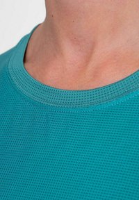 Camisa de malla de manga corta en color teal con un escote redondo y superficie texturizada, que presenta pequeñas perforaciones para mayor transpirabilidad.