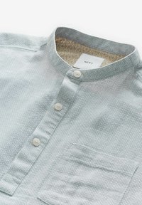 Chemise gris clair texturée avec col mandarin, trois boutons blancs, poche poitrine et doublure intérieure du col à motif.