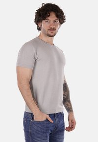 Camiseta gris claro de manga corta con un patrón texturizado, escote redondo y diseño ajustado, combinada con jeans azul oscuro.