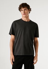 Tricou cu mâneci scurte din bumbac de culoare gri închis. Dispune de un guler rotund și o croială lejeră. Branding minimal detaliat pe față.